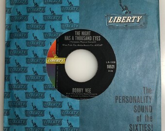 May include: A blue 45 RPM record sleeve with a black and white label. The label features the text "The Night Has A Thousand Eyes" by Bobby Vee. The sleeve has the text "The Personality Sound of the Sixties!" and the Liberty Records logo.