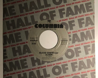 May include: A black and white 45 RPM vinyl record with a Columbia Records label. The record features the song "Alison" by Elvis Costello. The record is from October 1977.