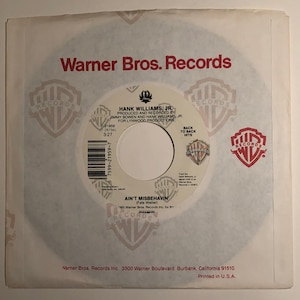Puede incluir: Un disco de vinilo de 7 pulgadas de Hank Williams Jr. titulado "Ain't Misbehavin'" (Fats Waller). El disco está en el sello Warner Bros. Records. El disco es rojo, blanco y azul con un logotipo de Warner Bros. Records en el centro.