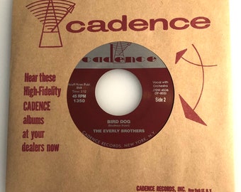 May include: A brown paper record sleeve with a red and white label. The label features the text "Cadence" and "Bird Dog" by "The Everly Brothers". The sleeve also includes the text "Hear these High-Fidelity CADENCE albums at your dealers now".