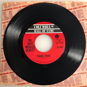May include: A black vinyl record with a red label. The label says "Columbia Hall of Fame" and features the song "Take Five" by The Dave Brubeck Quartet. The record was released in August 1960.
