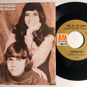 May include: A 45 RPM vinyl record by the Carpenters. The record is titled "For All We Know" and is from the movie "Lovers and Other Strangers". The record is on the AM Records label and has a catalog number of 1243.
