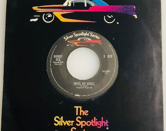May include: A black and white 45 RPM vinyl record with a black label. The label has the text "Silver Spotlight Series" in a white font. The record is titled "Devil or Angel" by Bobby Vee. The record is part of the "Silver Spotlight Series" and has the catalog number "X 020".