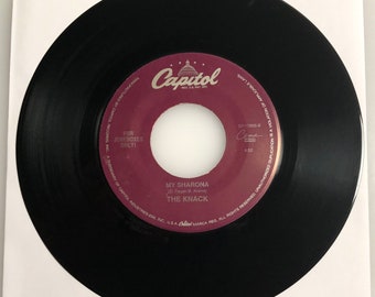 May include: A black vinyl record with a red label. The label has the text "Capitol" in white lettering and the text "My Sharona" in white lettering. The text "(D. Fieger-B. Averre)" and "The Knack" are also in white lettering. The record is for jukeboxes only.
