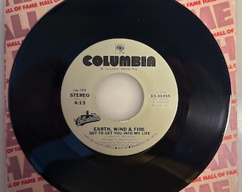 May include: A black vinyl record with a white and tan label featuring the text "COLUMBIA" and the song title "GOT TO GET YOU INTO MY LIFE" by Earth, Wind & Fire. The record is in a tan and pink sleeve with "HALL OF FAME" text.
