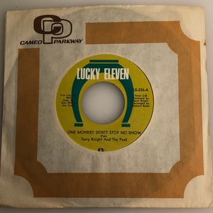 May include: A yellow and green vinyl record with the text "Lucky Eleven" and "One Monkey Don't Stop No Show (Tas) Terry Knight And The Pack" on the label. The record is on a white background.