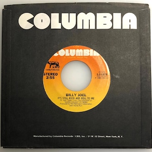Può includere: Un disco in vinile da 45 giri in bianco e nero di Billy Joel. Il disco è intitolato "It's Still Rock and Roll to Me" ed è tratto dall'album "Glass Houses".