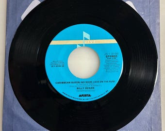 May include: A black vinyl record with a blue and white label featuring the text "Caribbean Queen (No More Love on the Run)" by Billy Ocean. The record is in a blue and white sleeve. The label also includes the Jive and Arista Records logos.