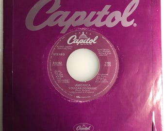May include: A purple vinyl record sleeve with a silver Capitol Records logo. The record is titled "America" by Russ Ballard and the song is "You Can Do Magic". The record is from the album "View From The Ground".