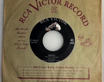 May include: A vintage RCA Victor 45 RPM record with a black label and a white center. The record is in its original tan paper sleeve, which features the RCA Victor logo and text. The record label reads "WANTED" by Perry Como.