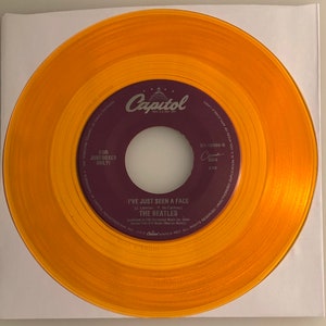 May include: A gold vinyl record with a purple label. The label has the text "Capitol" and "I've Just Seen A Face" by "The Beatles". The record is for jukeboxes only.