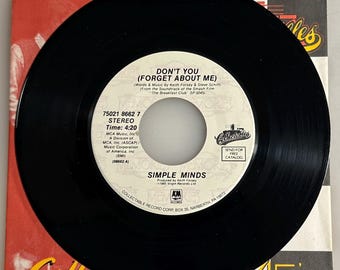 May include: A black vinyl record with the song title "Don't You (Forget About Me)" by Simple Minds. The record is in its original sleeve, which has a red and white design with the word "Memories" and the number "45's".