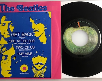 May include: A vintage vinyl record and sleeve featuring The Beatles. The sleeve is pink with blue text and yellow portraits of the band members. Song titles include "Get Back" and "Two of Us". The record label is green with the band's name and an apple graphic.