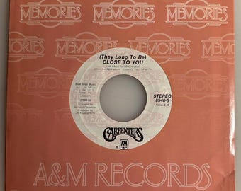 May include: A vintage vinyl record for the song "Close to You" by The Carpenters. The record label is white with black text and the record sleeve is peach-colored with the word "MEMORIES" repeated. The A&M Records logo is visible.