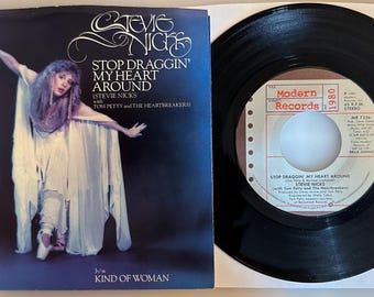 May include: A vintage vinyl record and album cover for Stevie Nicks' song "Stop Draggin' My Heart Around" featuring Tom Petty and The Heartbreakers. The album cover shows a woman in a flowing white dress. The record is black.