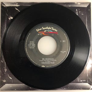 May include: A black vinyl record with a white label. The label has the text "Silver Spotlight Series", "Mitty Gritty Dirt Band", "Released 11/76", "Chart # 5", "X 061", "MR. BOJANGLES", "(Producer:  Buddy Charles & His Dog Teddy)", "Capitol Records, Inc. A Subsidiary of Capitol Industries, Inc. U.S.A. Marca Reg. MFD. All Rights Reserved.", and "ANC 41515".