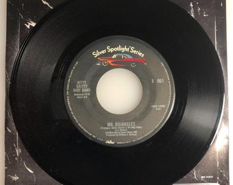 May include: A black vinyl record with a white label. The label has the text "Silver Spotlight Series", "Mitty Gritty Dirt Band", "Released 11/76", "Chart # 5", "X 061", "MR. BOJANGLES", "(Producer:  Buddy Charles & His Dog Teddy)", "Capitol Records, Inc. A Subsidiary of Capitol Industries, Inc. U.S.A. Marca Reg. MFD. All Rights Reserved.", and "ANC 41515".