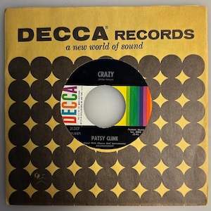 May include: Vintage DECCA RECORDS 45 RPM record featuring Patsy Cline's song "Crazy." The record is in a yellow sleeve with a repeating pattern of brown circles and the DECCA Records logo. The record label is black with a colorful stripe.