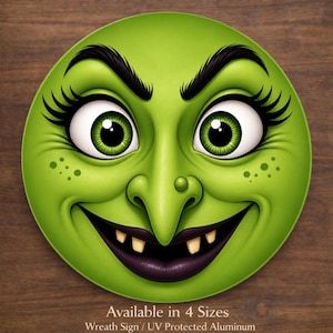 May include: A circular aluminum wreath sign featuring a cartoon witch face with bright green skin, large expressive eyes with long black eyelashes, a prominent nose with a wart, and a wide grin showing two yellow teeth and dark purple lips.
