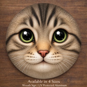 May include: A circular sign displaying a detailed illustration of a cat's face with large green eyes, a pink nose, and a light brown and grey striped pattern. The text "Available in 4 Sizes" and "Wreath Sign / UV Protected Aluminum" is at the bottom.