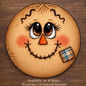 May include: A round sign featuring a tan burlap-textured scarecrow face with large brown eyes, long eyelashes, a triangular orange nose, and a stitched smile. A blue and white plaid patch is on the cheek. Text reads: Available in 4 Sizes.
