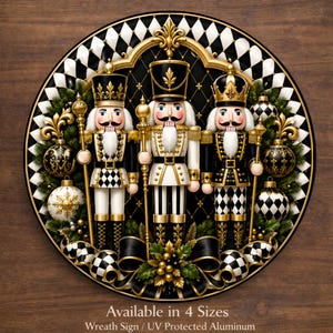 May include: A round aluminum wreath sign featuring three nutcrackers in black, white, and gold uniforms. The design includes a harlequin pattern border, decorative ornaments, and greenery. Text at the bottom reads: Available in 4 Sizes Wreath Sign / UV Protected Aluminum.