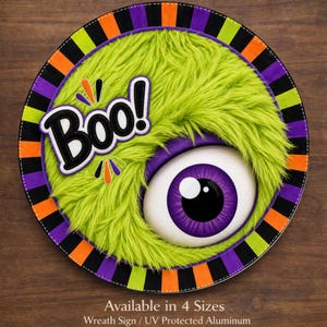 May include: Round Halloween wreath sign featuring a green furry monster with a large purple eye. The word "Boo!" is in a white and black bubble. The sign has a black, orange, green, and purple border.