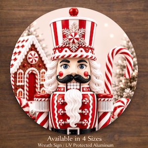 May include: A festive, round Christmas wreath sign featuring a detailed nutcracker soldier with a red and white striped hat and uniform. The sign includes a gingerbread house and candy cane accents. Text: Available in 4 Sizes. Wreath Sign / UV Protected Aluminum.