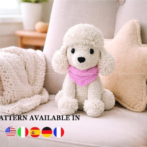 Puede incluir: Un caniche blanco de ganchillo con una bufanda rosa está sentado en una silla color crema junto a un cojín en forma de estrella. Una manta color crema está sobre el brazo de la silla. El texto "PATTERN AVAILABLE IN" se muestra en la parte inferior.
