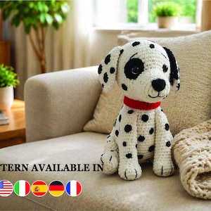 May include: A crocheted Dalmatian dog with black spots, a red collar, and black eyes. The dog is sitting on a beige sofa. The text "PATTERN AVAILABLE IN" is visible with flags.