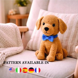 May include: A crocheted golden-brown puppy dog with a blue bow tie sits on a chair. The dog has black eyes and a black nose. The text "PATTERN AVAILABLE IN" is visible at the bottom of the image.