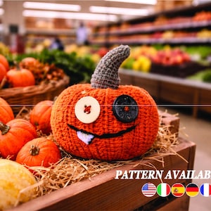 May include: An orange crocheted pumpkin with a grey stem and button eyes, displayed in a wooden crate with other pumpkins. The pumpkin has a stitched smile and a single tooth. Text on the image reads "PATTERN AVAILABLE IN".