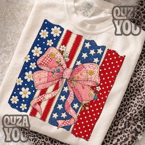 Op de afbeelding: Wit Comfort Colors sweatshirt met een patriottisch ontwerp. Het ontwerp toont een roze strik met bloemaccenten, tegen een achtergrond van blauw met witte madeliefjes, rode strepen en rode stippen. Het ontwerp doet denken aan de Amerikaanse vlag.
