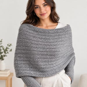 May include: A grey knit poncho featuring a textured horizontal ribbed pattern and long sleeves. The garment is crafted from a heathered yarn blend, showcasing a wide neckline that drapes over the shoulders, providing a layered look over a white top.