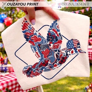 May include: A cream-coloured fabric featuring a patriotic duck design. The duck wears a baseball cap with an American flag pattern and has wings with a patchwork of red, white, and blue patterns. The text "OUZAYOU PRINT" and "ORIGINAL DESIGNER" are visible.
