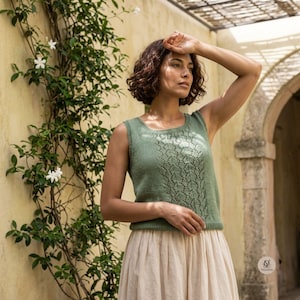 May include: A sage green sleeveless knit top featuring a vertical lace pattern down the centre front, a round neckline, and ribbed trim at the armholes and hem, paired with a long, flowing cream-coloured skirt made of a lightweight fabric.