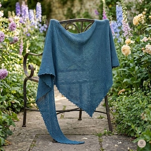 Könnte beinhalten: Ein dreieckiges, blaugrünes Stricktuch mit einer strukturierten kraus rechts gestrickten Oberfläche und einem zarten, wellenförmigen Rand. Das Tuch liegt über einem dunklen Metall-Gartenstuhl und zeigt seinen weichen Stoff sowie die langgezogenen, spitzen Enden.