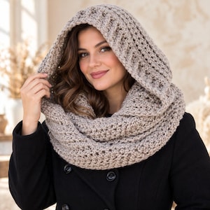 May include: A beige crochet hooded cowl featuring a thick, textured knit pattern. The accessory is designed to drape around the neck and shoulders, with an integrated hood that provides coverage. The yarn has a neutral, light brown tone.