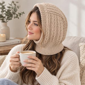Pode incluir: Uma balaclava de malha bege com um padrão de tranças verticais e uma gola canelada. O acessório é feito de um fio macio e texturizado, proporcionando cobertura total para a cabeça e o pescoço com uma abertura larga para o rosto.