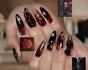 May include: Almond-shaped nails featuring a clear base with dark red and black ink-like swirls, accented with black 3D embellishments, small metallic beads, and thin black line art. The design incorporates small inset images of Silent Hill.