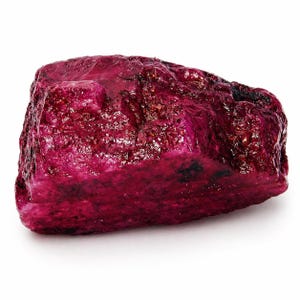 May include: A rough, uncut ruby gemstone with a deep red-purple hue. The surface has a textured, uneven appearance with areas of darker coloration. The gemstone is displayed against a white background, highlighting its natural form and color.