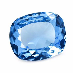 May include: A cushion-cut gemstone with a vibrant sky-blue color and a faceted surface. The stone features a rectangular shape with rounded corners and a polished finish that reflects light across its multiple geometric facets and edges.
