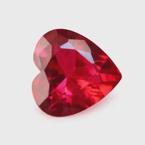 May include: A heart-shaped gemstone with a vibrant, deep red colour and a faceted surface. The stone features multiple triangular and kite-shaped facets that reflect light, creating a brilliant, sparkling appearance with varying shades of red.