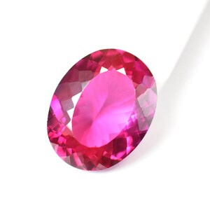 Op de afbeelding: Een levendige, ovaal geslepen edelsteen met een diepe magenta en felroze kleur. De steen heeft een gefacetteerd oppervlak dat een briljante, reflecterende uitstraling creëert met geometrische patronen vanuit het midden.
