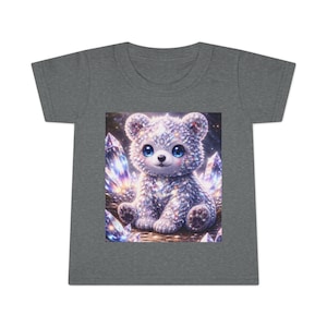 Pode incluir: Camiseta cinza para crianças pequenas com um urso de desenho animado com pelo brilhante e olhos azuis. O urso é cercado por cristais coloridos. O desenho está centralizado na frente da camiseta.