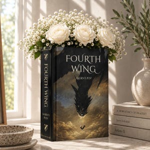 Könnte beinhalten: Ein gebundenes Buch mit dem Titel Fourth Wing Xaden's POV und einem dunklen Cover-Motiv, das einen Drachen zeigt, der auf eine kleine Figur herabsteigt. Das Buch ist mit einem Strauß aus weißen Rosen und Schleierkraut verziert und steht aufrecht.