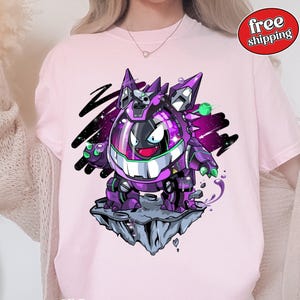 Puede incluir: Camiseta rosa claro con un personaje de dibujos animados morado y negro con una gran sonrisa y elementos robóticos. El personaje está sobre una formación rocosa flotante sobre un fondo estrellado. La camiseta tiene cuello redondo.