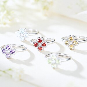 May include: Five silver rings, each featuring a four-leaf clover design set with small, round, faceted gemstones in purple, light blue, red, yellow, and pale green. Each ring has a thin, polished silver band and a delicate, textured metal setting.