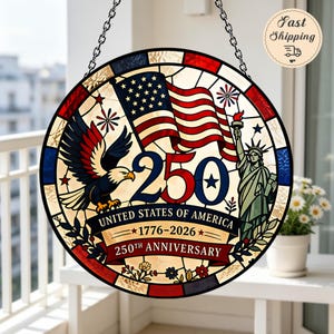 Könnte beinhalten: Ein runder Buntglas-Suncatcher mit einem Weißkopfseeadler, der Freiheitsstatue und einer amerikanischen Flagge. Das Design enthält den Text 250, UNITED STATES OF AMERICA, 1776-2026 und 250TH ANNIVERSARY in den Farben Rot, Weiß und Blau mit Kette.