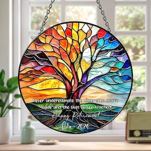 May include: A circular stained glass window depicting a tree, with a palette of red, orange, yellow, blue, and green. The text reads "Never underestimate the difference you've made and the lives you've touched! Happy Retirement, Dila - 2026". It is suspended by a chain.